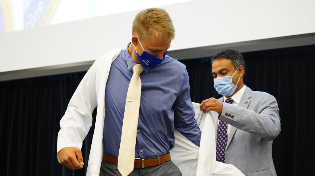 Pavan Brahmamdam, M.D., (right) helps Austin Kantola into his white coat. Kantola is one of the Class of 2025 who will be mentored by Brahmamdam during the next four years through OUWB's PRISM program.