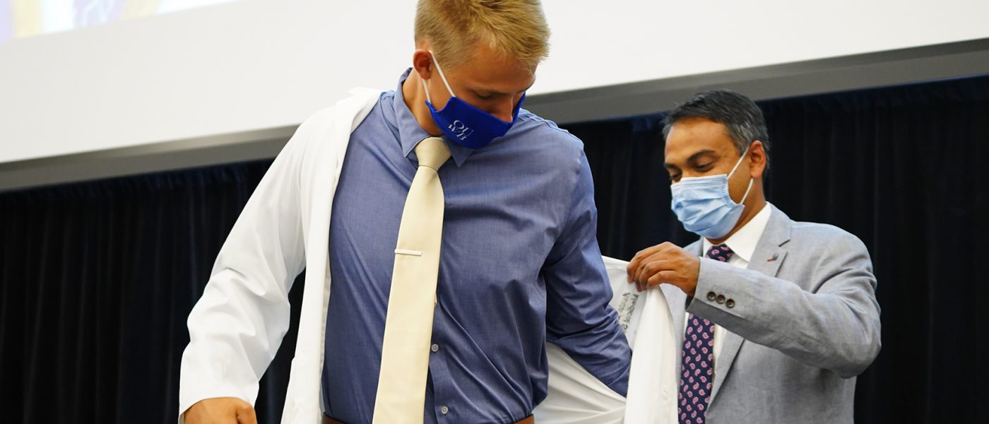 Pavan Brahmamdam, M.D., (right) helps Austin Kantola into his white coat. Kantola is one of the Class of 2025 who will be mentored by Brahmamdam during the next four years through OUWB's PRISM program.