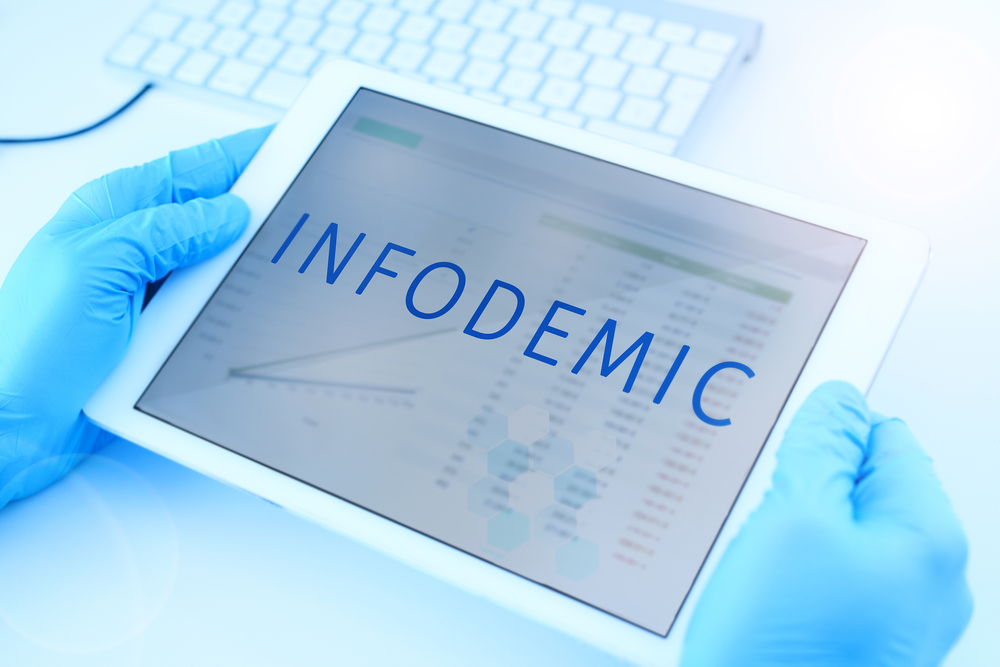 closeup of tablet that reads infodemic and is held by a doctor wearing gloves